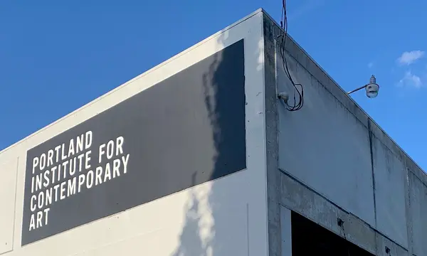 photograph of the upper right hand corner of PICA's building on a sunny day. white text is painted in a black box on the side of the building that reads 