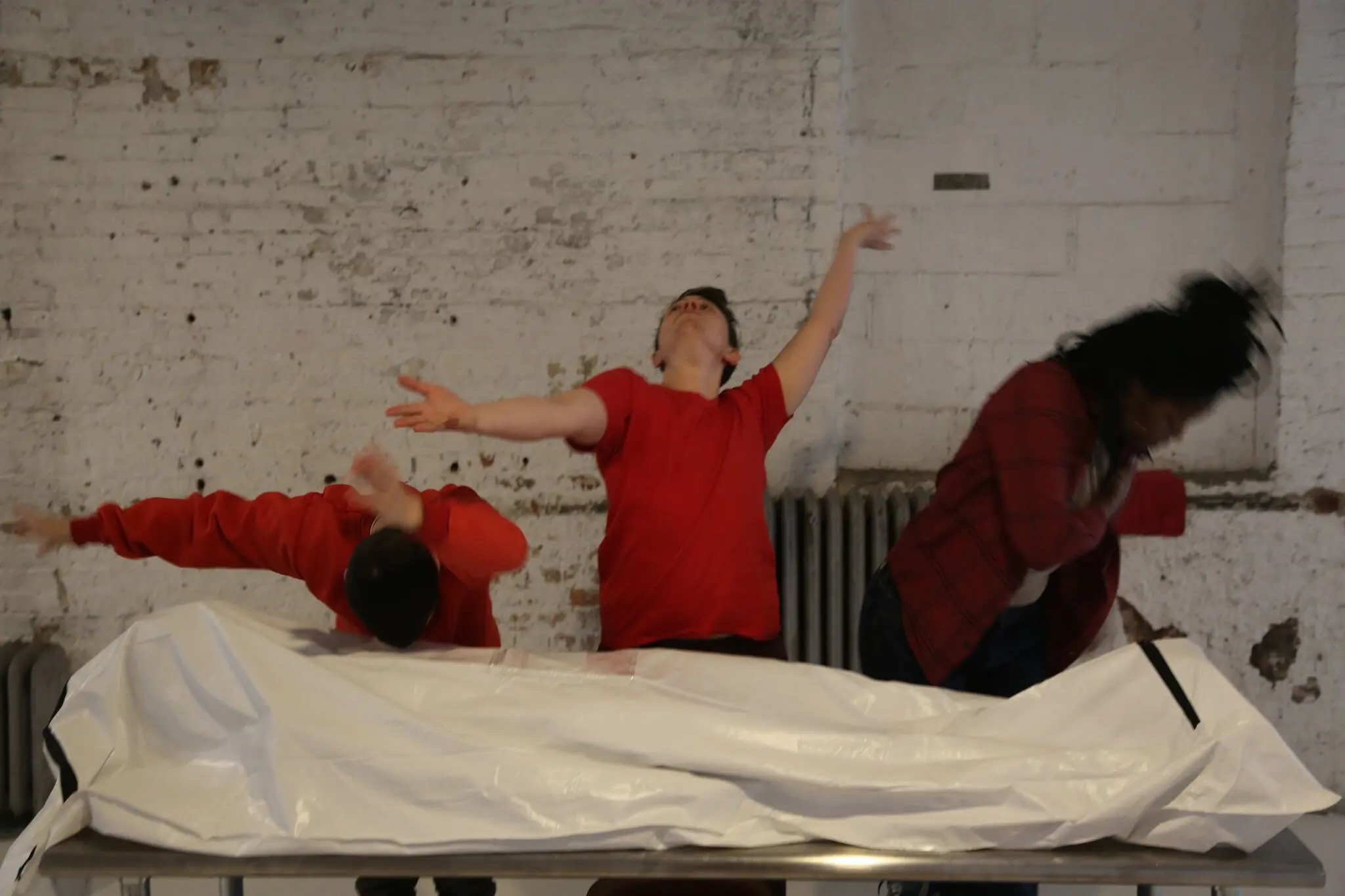 devvynn emory from nyt march 25 2021, shows three performers mid-moement all in red shirts over what looks like a white body bag  - 1.jpg