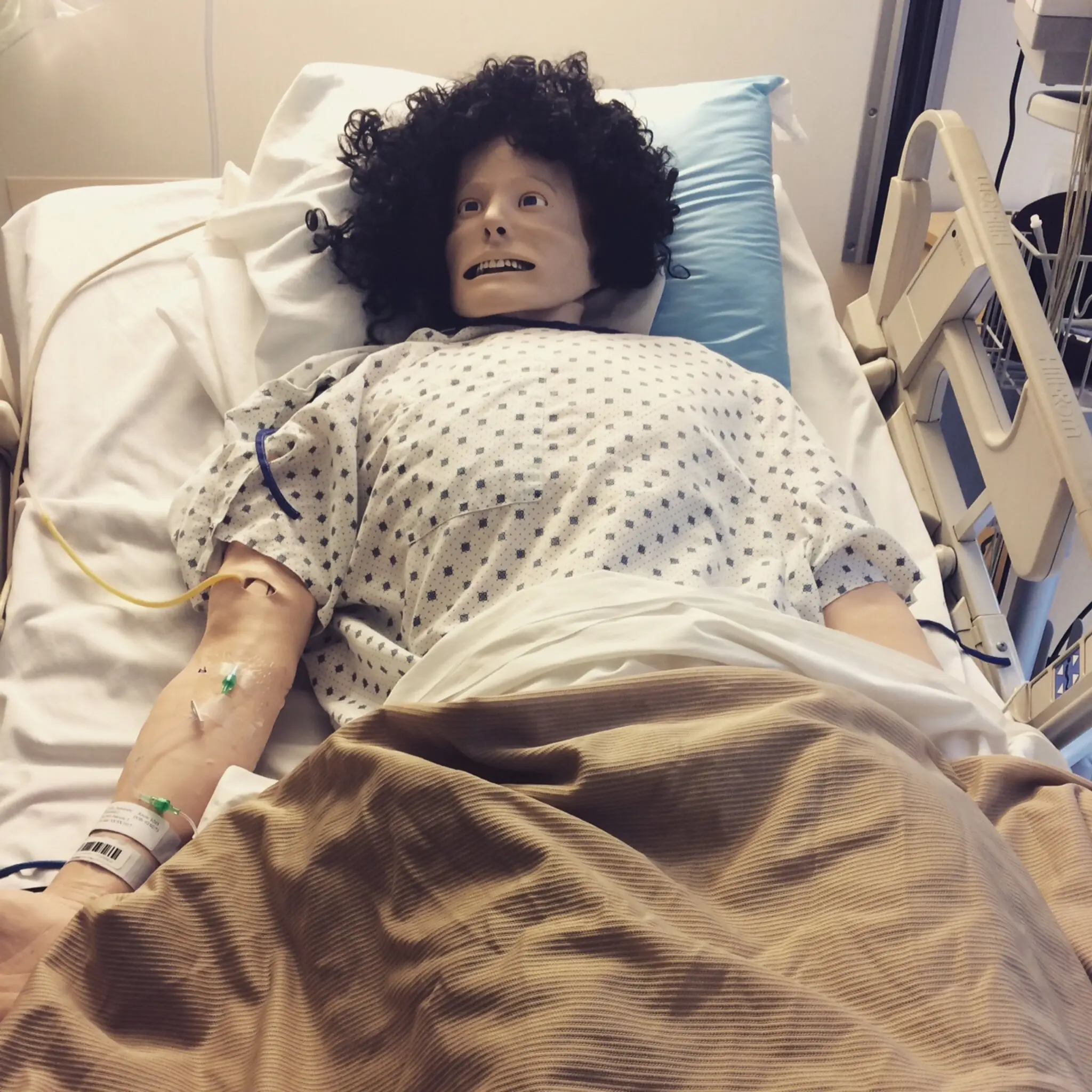 devynn emory from NYT article March 25 2021_3, a mannequin with a black curly wig and mask on in a hospital bed with an IV in left arm.jpg