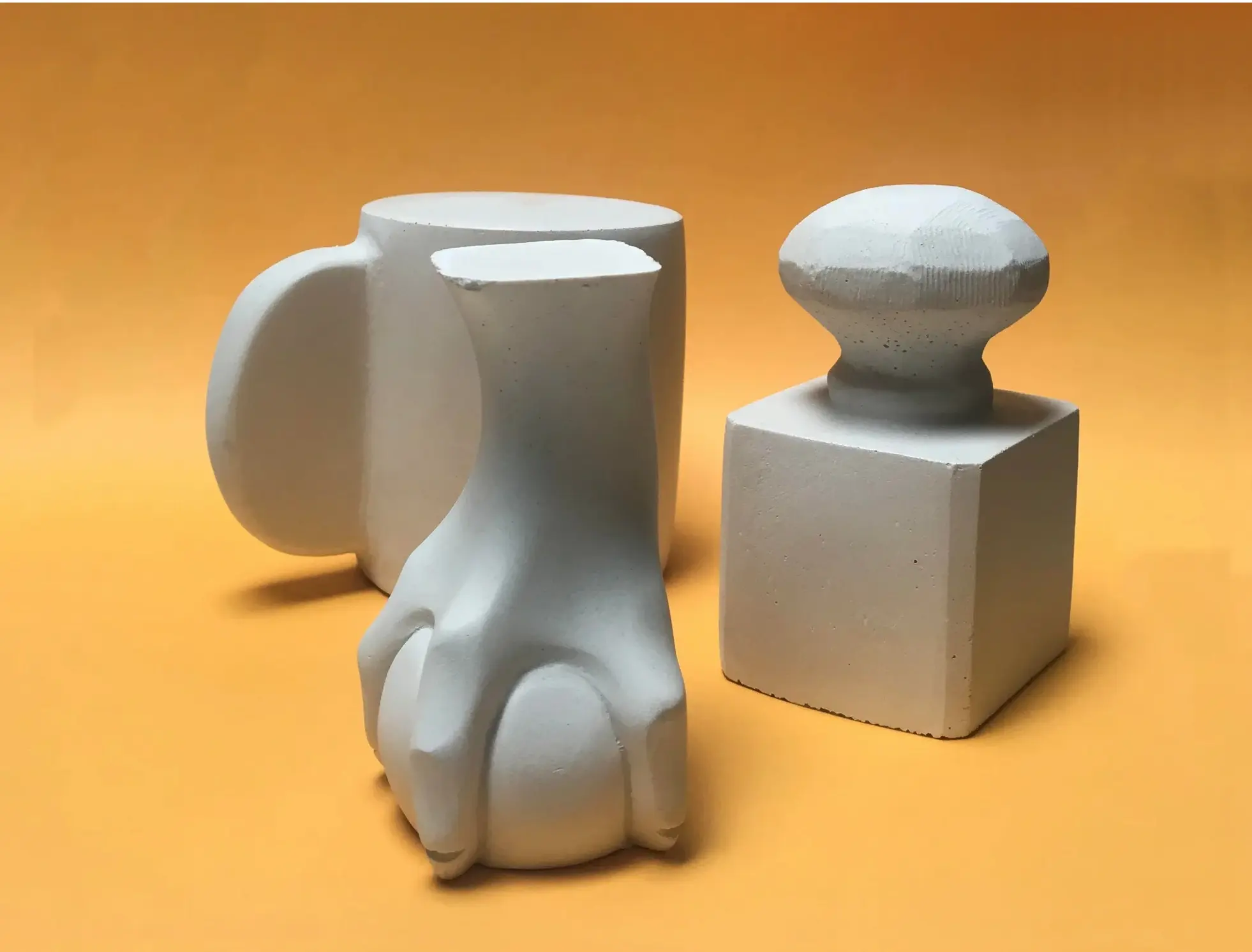 three concrete paperweights, art objects by gordon hall, on a yellow seamless background