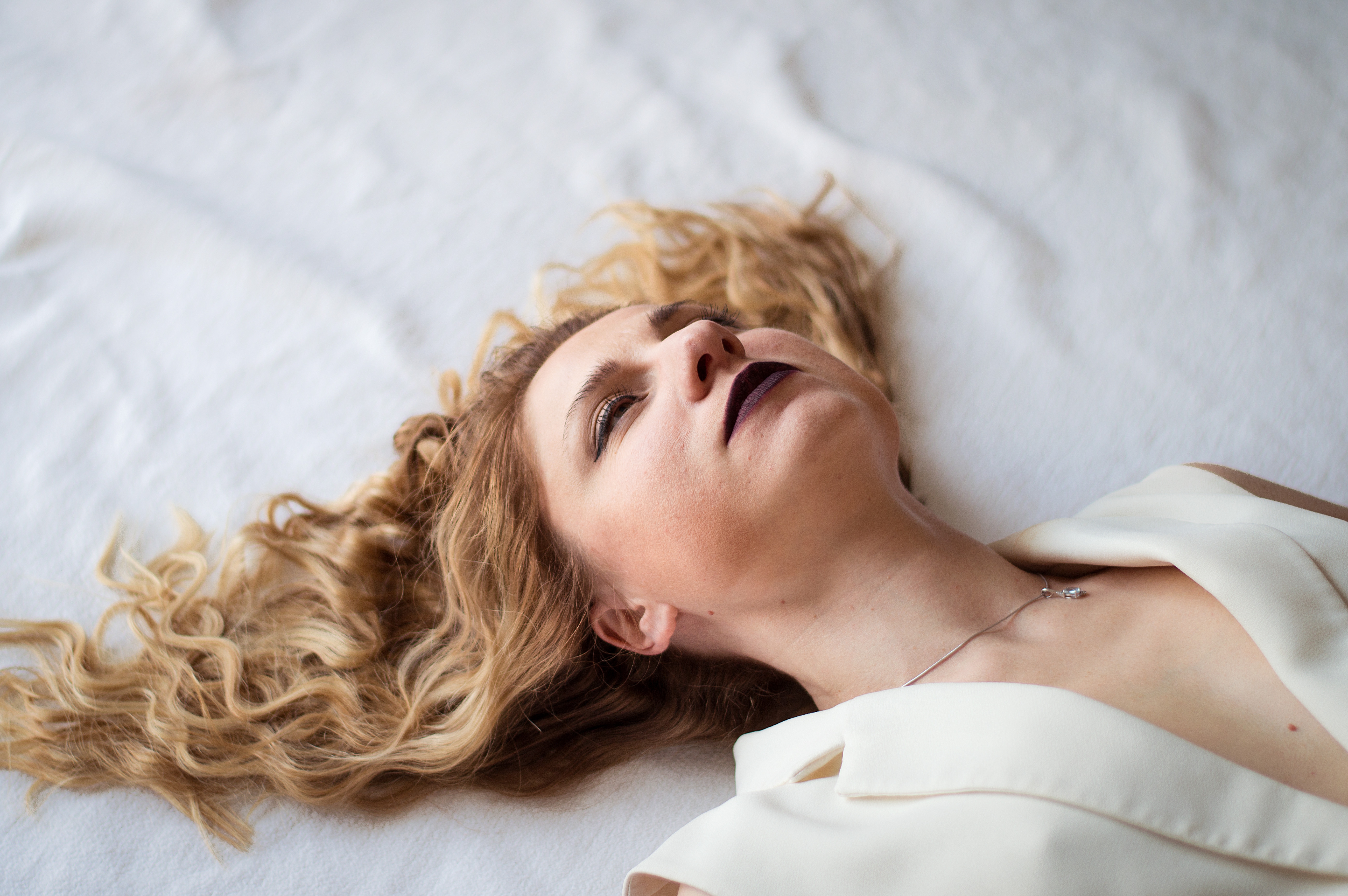 woman-with-curly-hair-and-makeup-lying-on-white-sheet.jpg