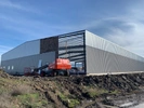 Metal warehouse building under construction. There is a red sky lift sitting in the front not being used. 