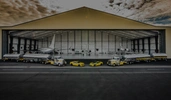 Large aircraft hangar filled with planes, trucks, and yellow sports cars