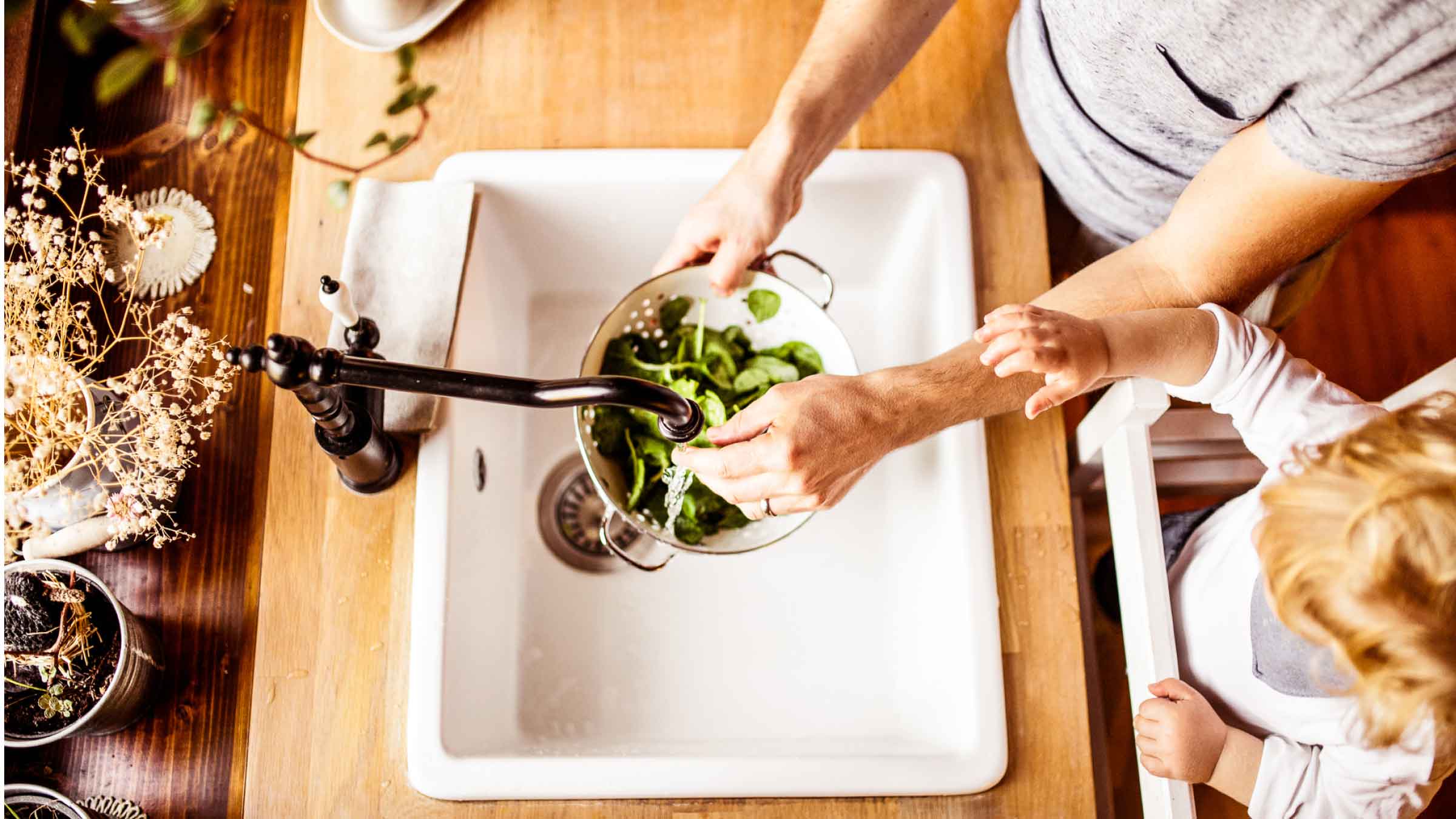 Ariel view of father and toddler washing a colander of spinach in an old farmhouse style kitchen sink.