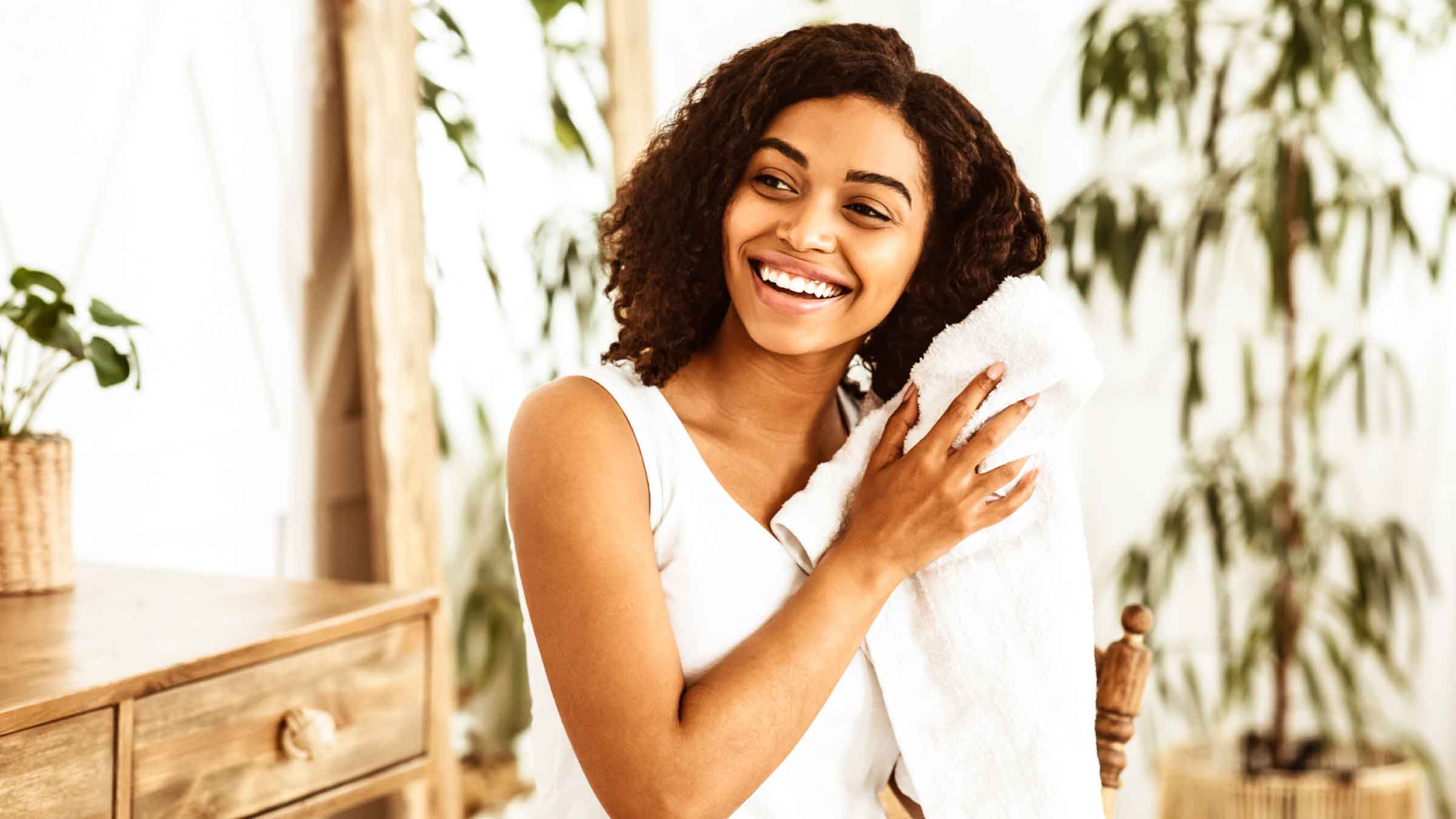 Young woman smiles as she towel dries her wet hair, in a light filled bathroom.