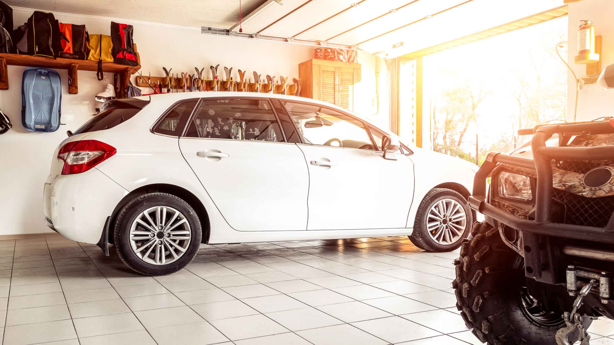 Small white car, parked in a modern well organised garage with open electric roller door.