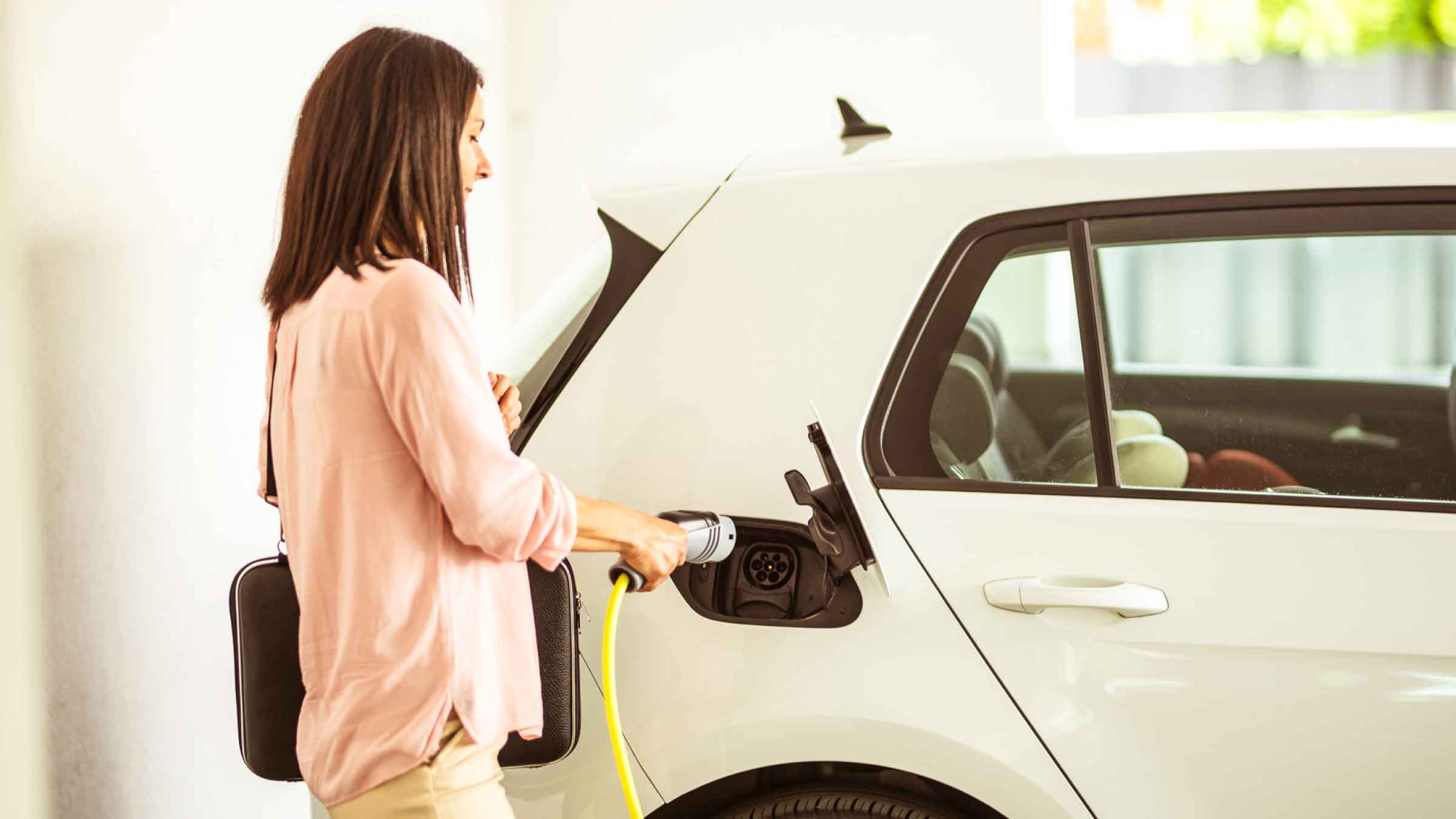 Woman in garage, about to plug in her electric vehicle.