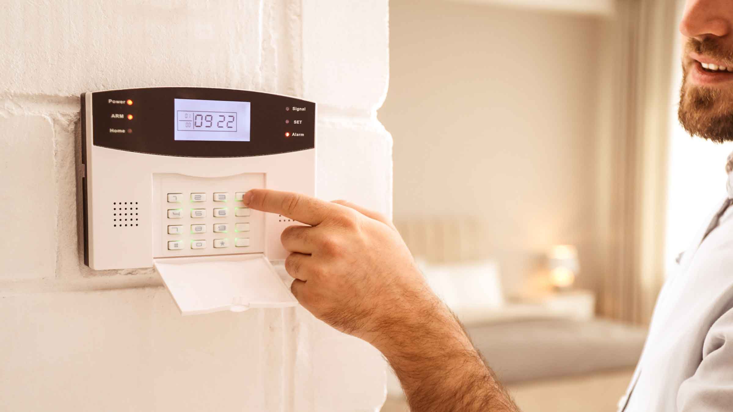 Man about to type on the keypad of a security device mounted to wall in his home.