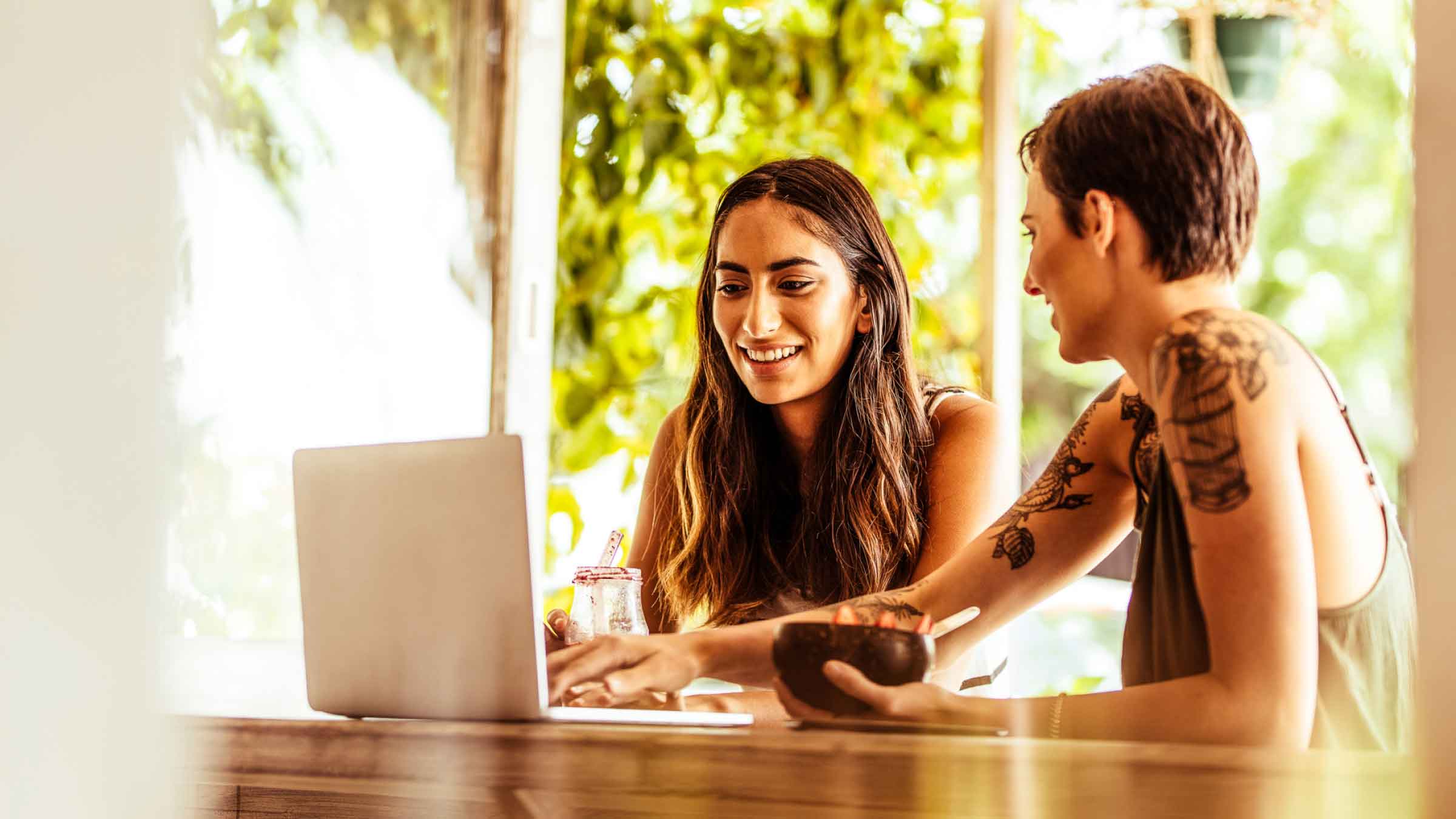 Two women sitting at a table eating breakfast while looking intently at a laptop.