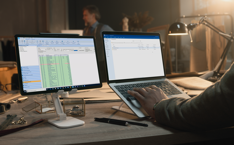 Person at desk with monitor and laptop SmartAccounting Cost Report and Scenechronize on screens