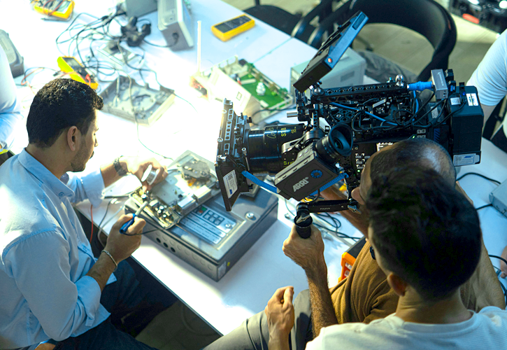 Camera person filming person sitting with computer tech equipment hard drives