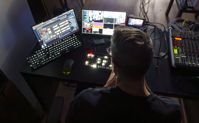 Production team member reviewing a multi-screen dashboard alongside broadcast and audio equipment.