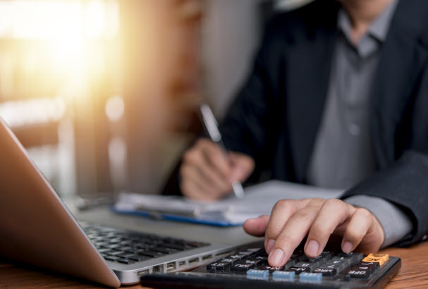 Close up of person's hand on calculator next to laptop