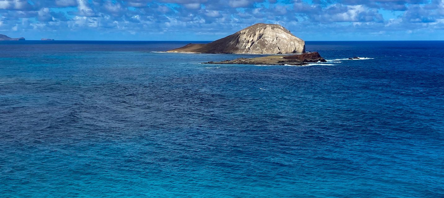 Rabbit Island (Mānana Island) off the coast of Oahu, Hawaii, surrounded by deep blue ocean waters with a partly cloudy sky overhead.