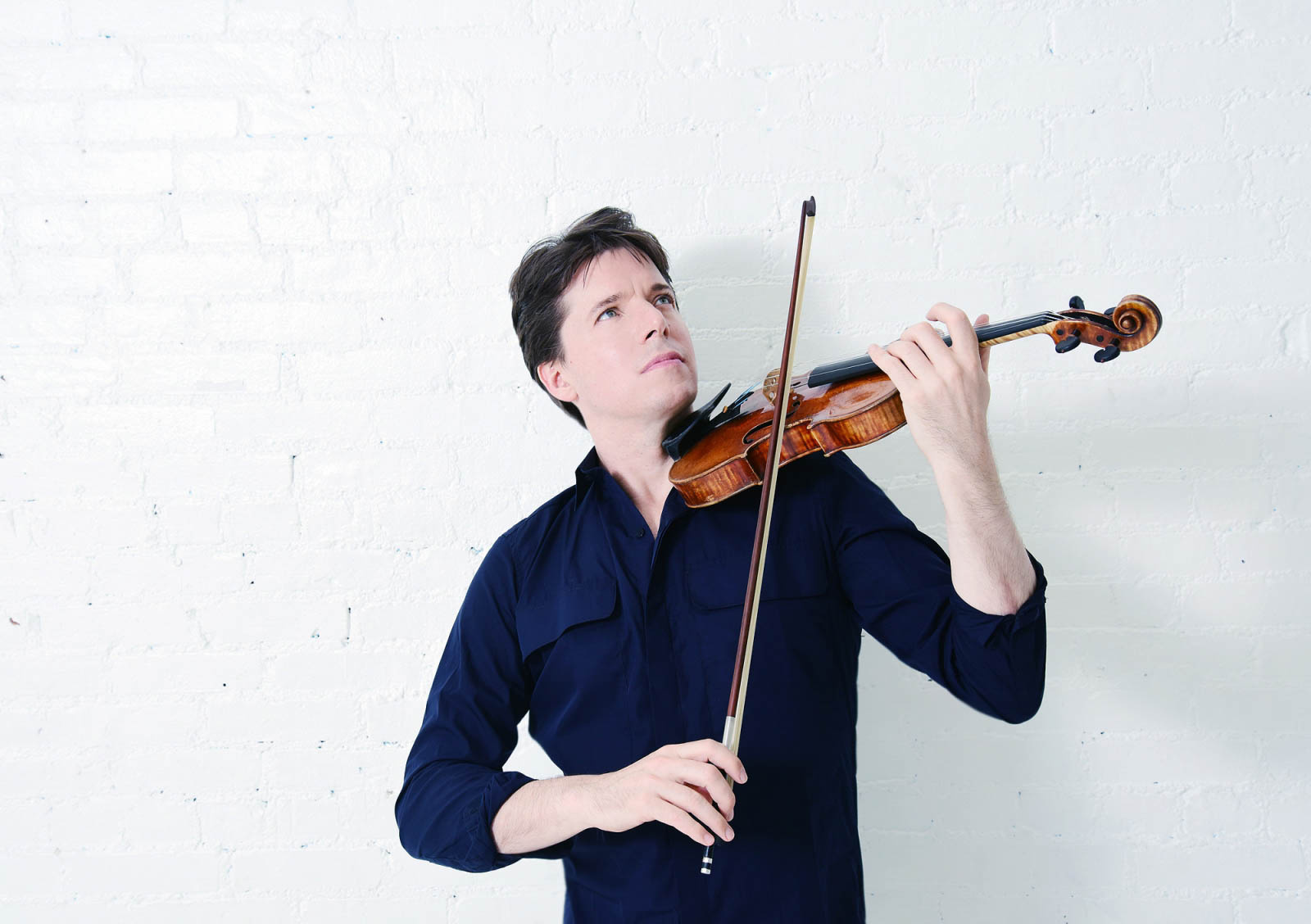 Joshua Bell playing a violin against a white backdrop. 