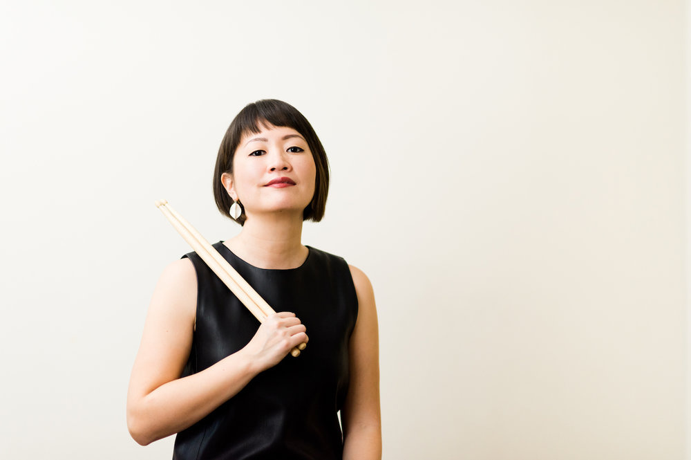 Haruka Fujii holding drum sticks over her shoulder in front of a cream backdrop. 