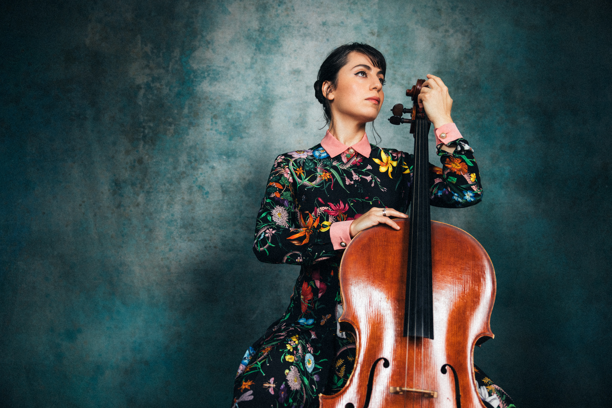 Karen Ouzounian holding a cello against a dark blue backdrop. 