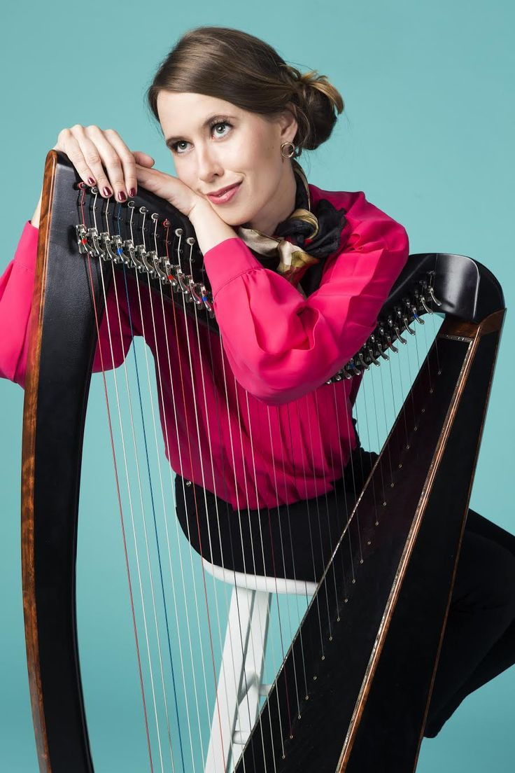 Maeve Gilchrist leaning on a harp with a light blue backdrop. 