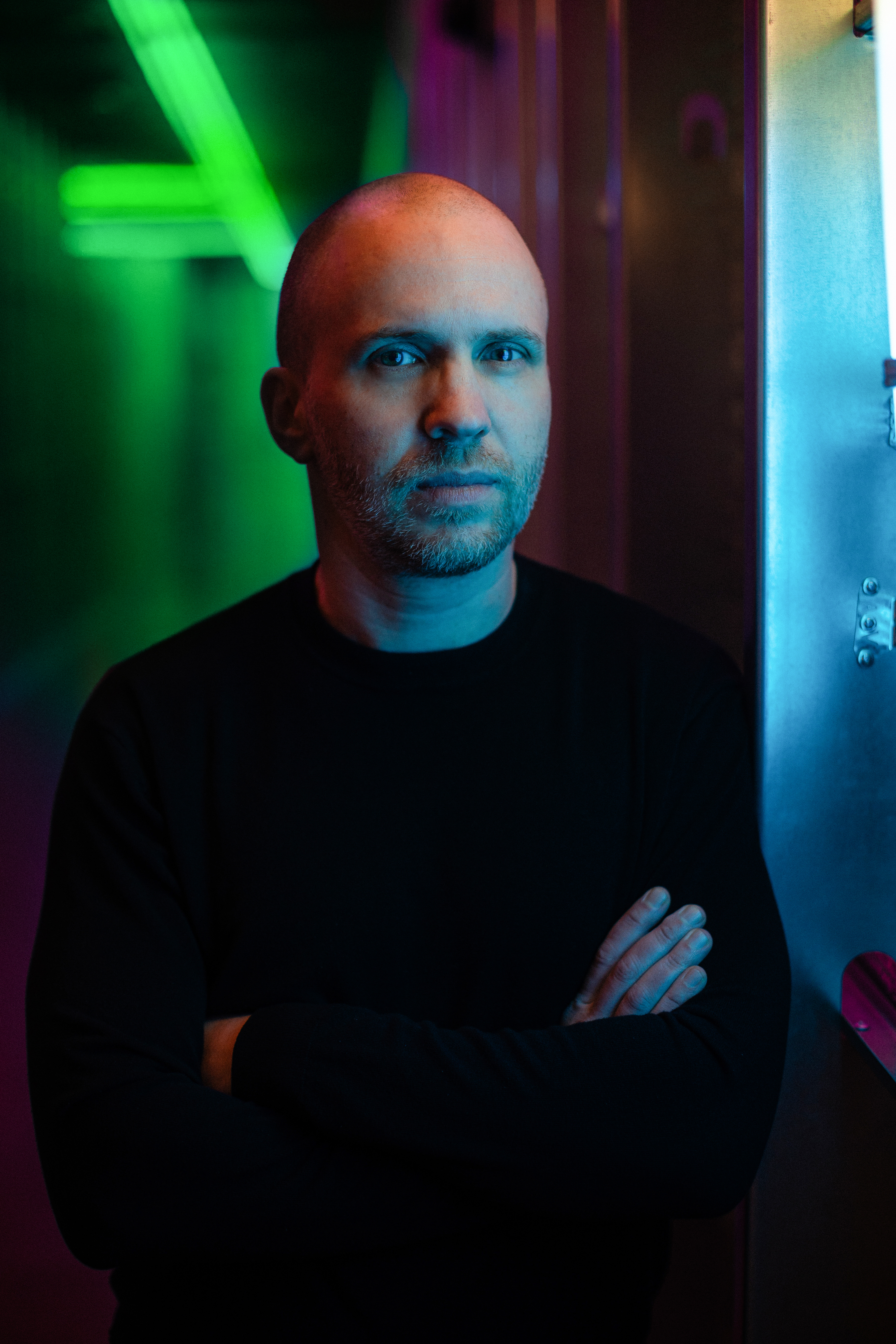 A photo of David Danzmayr standing with his arms folded with a dramatic green background.