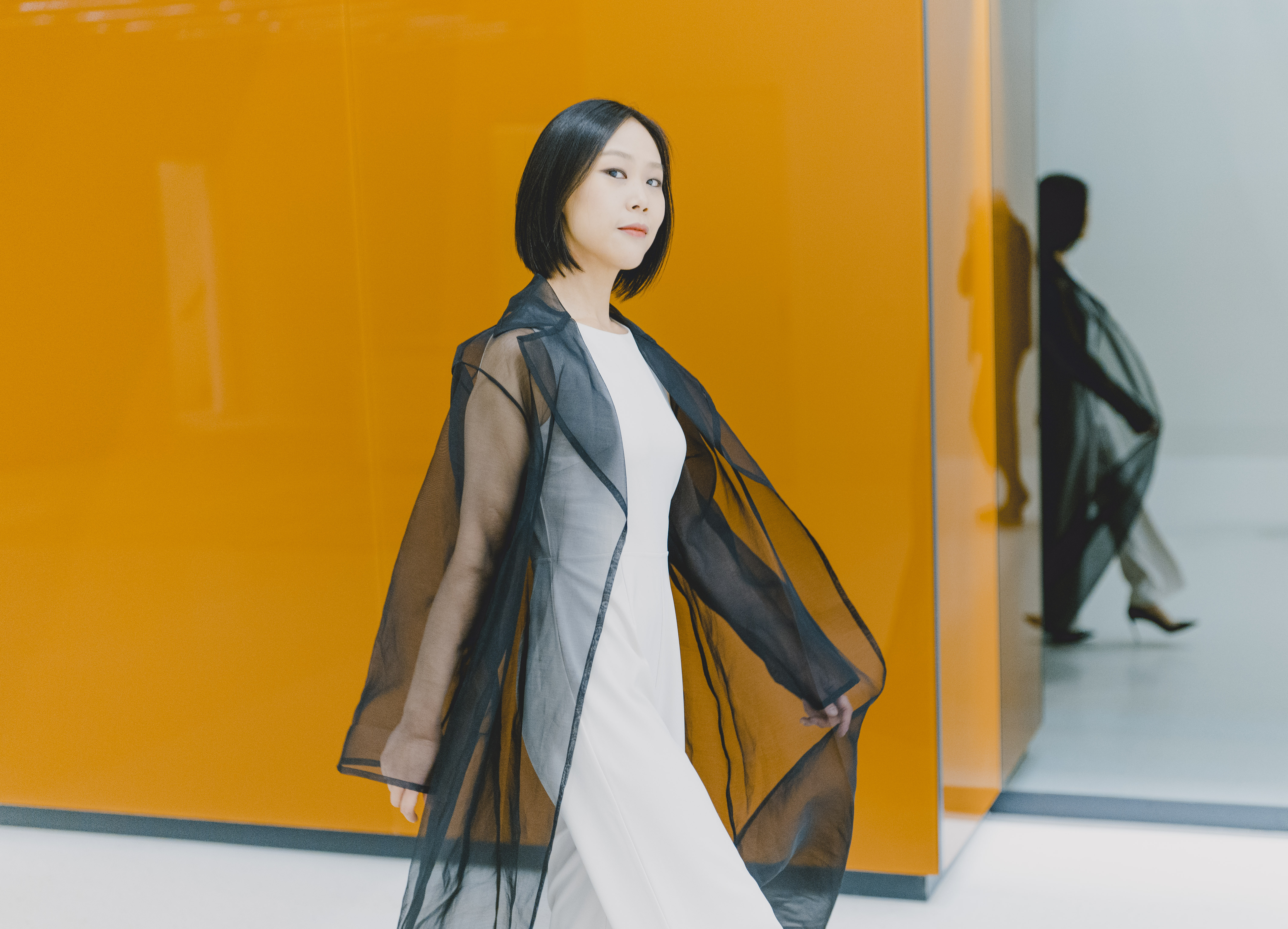 Yeol Eum Sol walking in front of a vibrant yellowish orange wall.