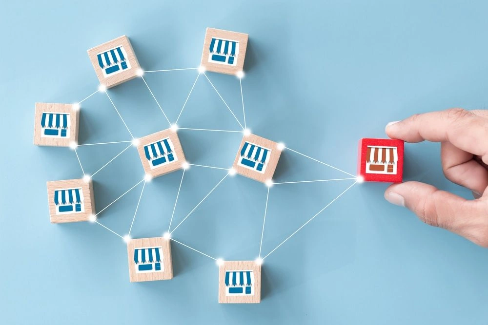 Wooden blocks marked with storefront icons connected in a network, representing franchise locations