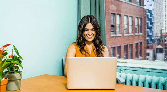 Happy woman sitting at table looking at laptop