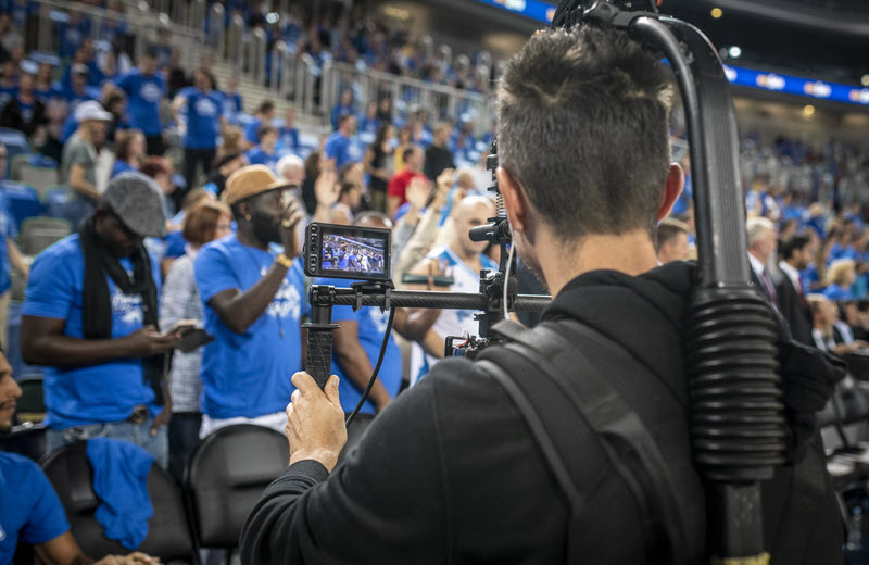 Cameraman with a body-mounted camera rig filming a large crowd at a stadium production shoot