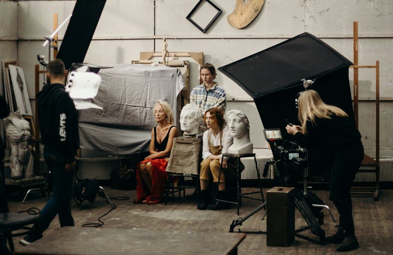 Film crew and actors during a production shoot in an artist's studio with sculptures and professional lighting