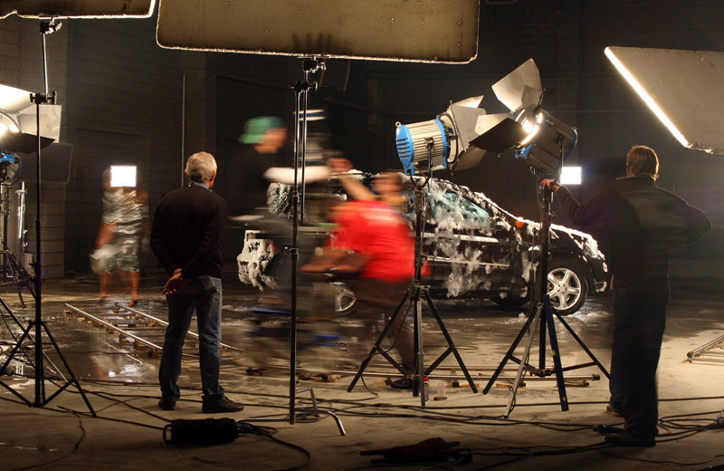 Film crew and actors during a large-scale commercial studio production shoot with professional lighting and motion blur