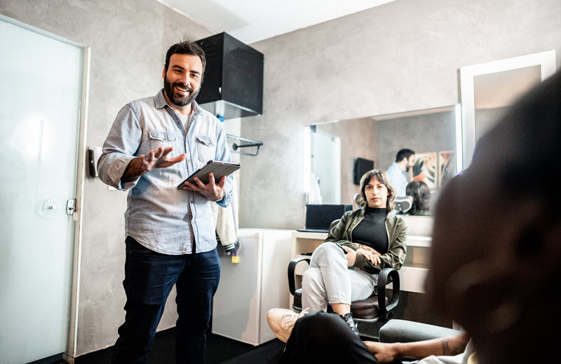 Production coordinator holding a tablet speaking with two background actors in a makeup room before a filming day