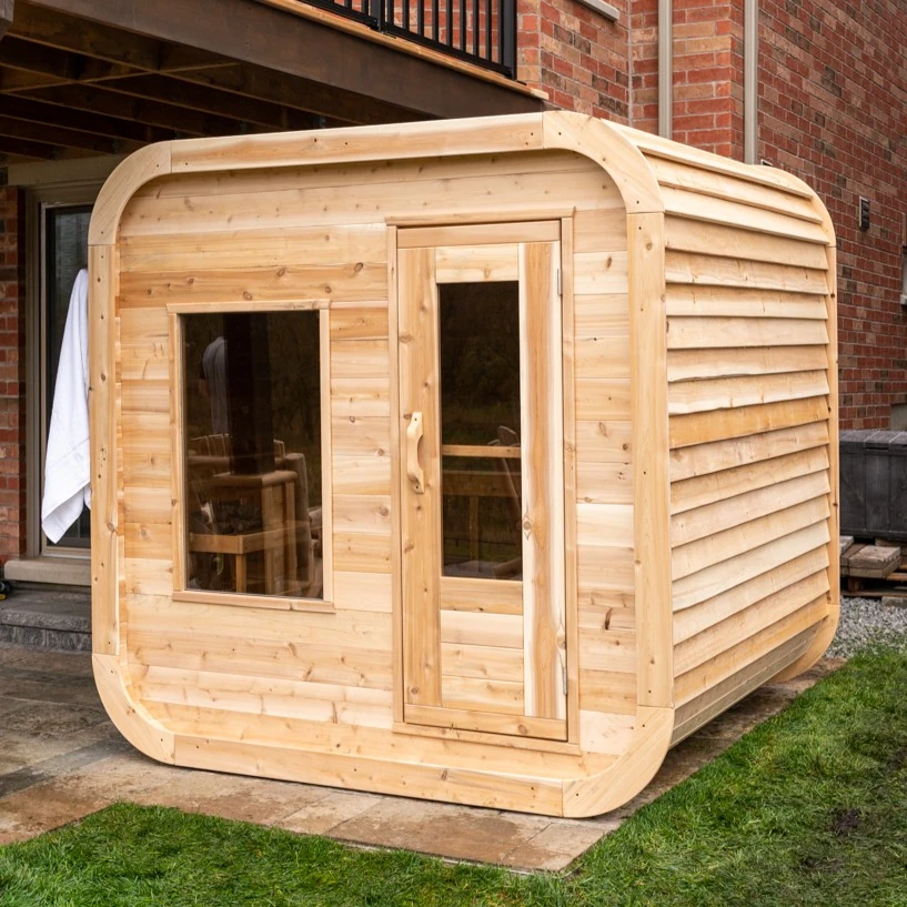 A LeisureCraft Luna cabin sauna built in eastern white cedar, lighter and paler in tone, on a backyard patio.