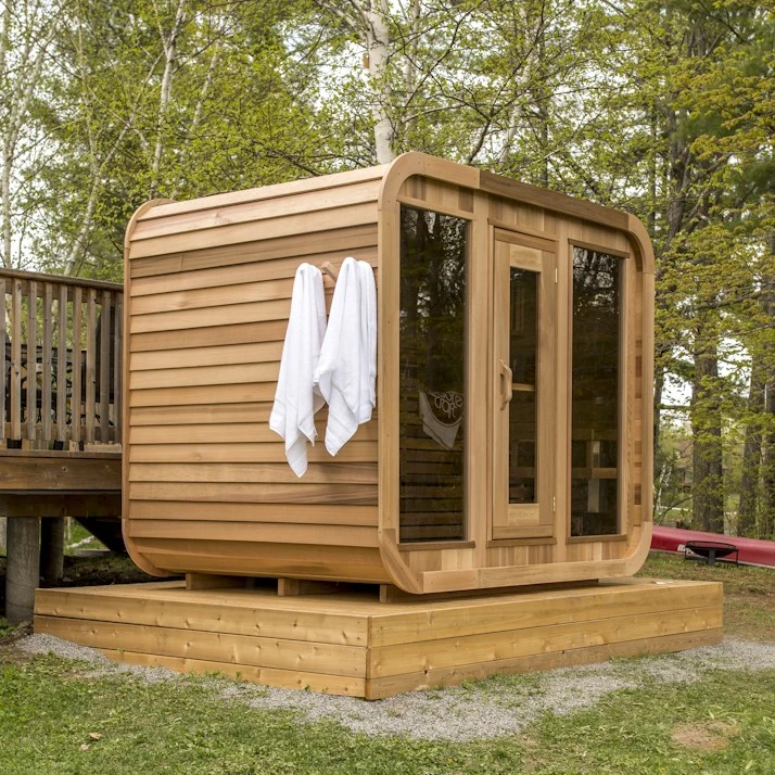 A LeisureCraft Luna cabin sauna built in clear western red cedar, warm reddish-brown tone, on a lakeside deck.