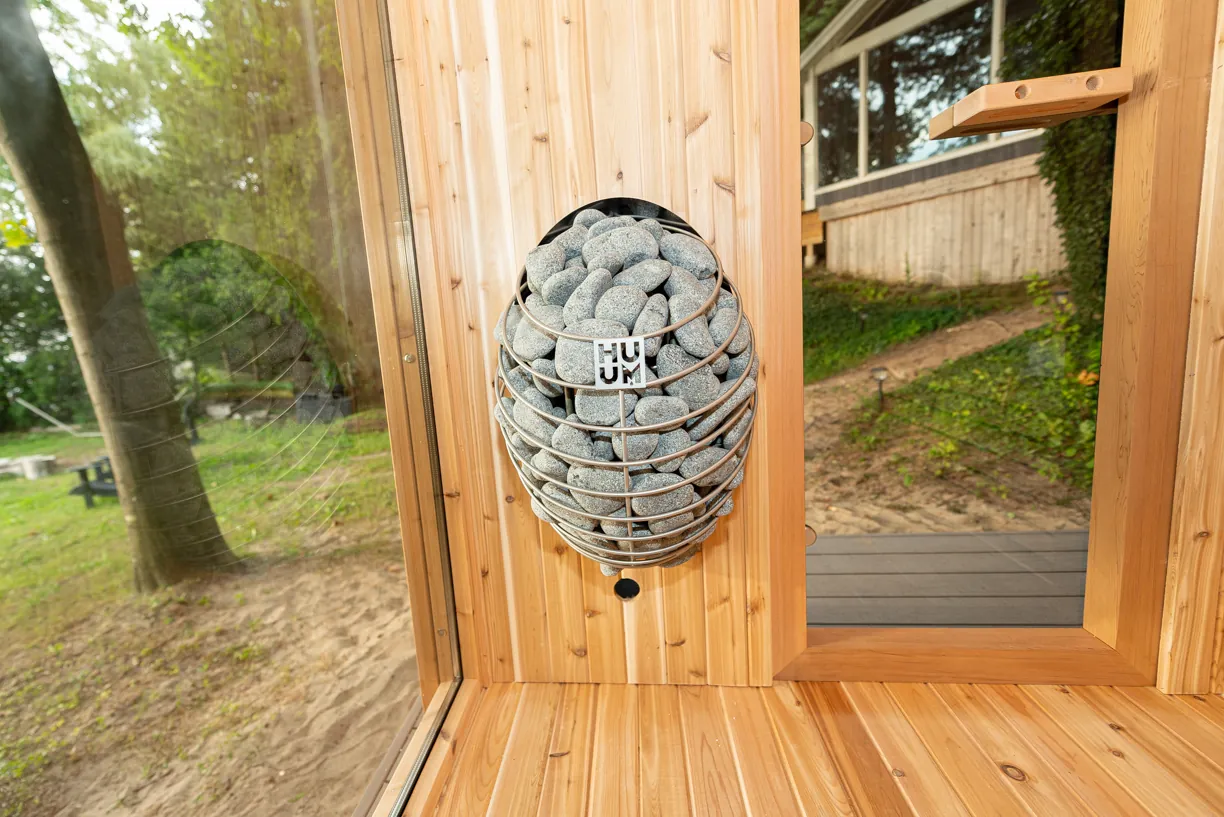 HUUM sauna heater with stacked stones in a wire cage, mounted on a cedar wall next to the door