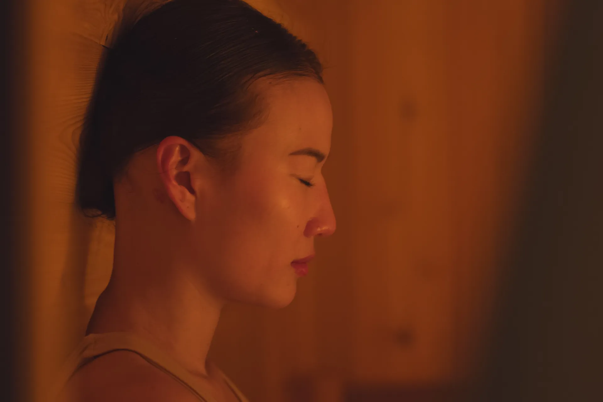 Close-up profile of a woman with her eyes closed, resting peacefully in the warm glow of a sauna