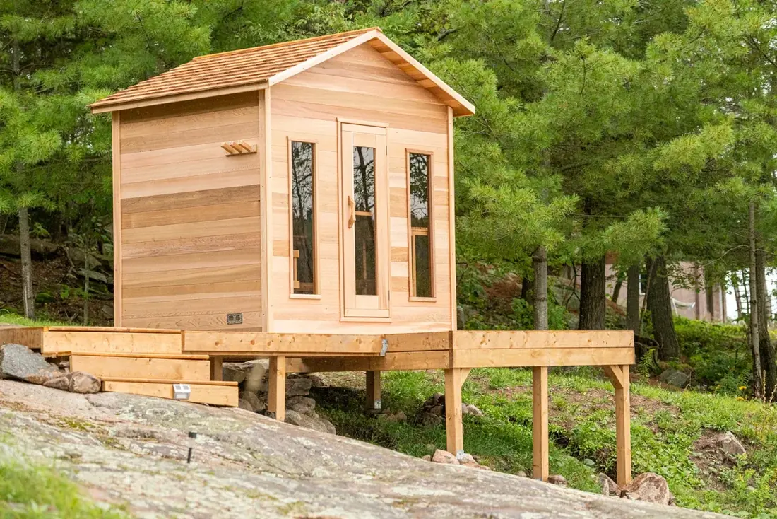 LeisureCraft cabin sauna in western red cedar with tongue-and-groove walls, dovetail corners, and a glass door, set at a Canadian cottage