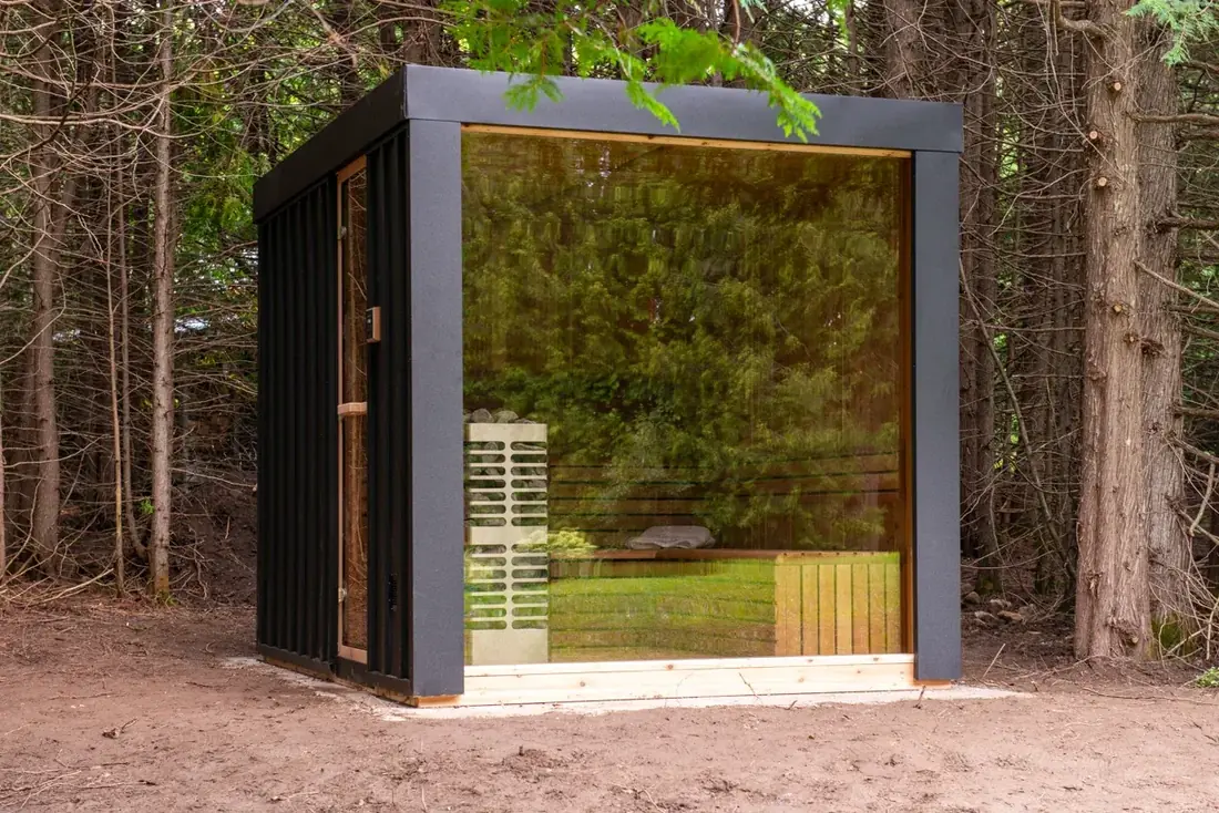 LeisureCraft Pure Cube sauna with large glass panels and black metal siding, contemporary modular design in an outdoor setting