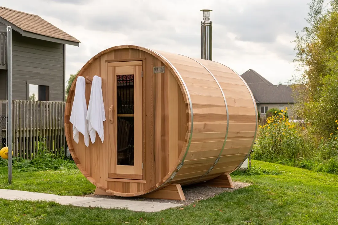 LeisureCraft barrel sauna in western red cedar with curved staves and stainless steel bands, set in a wooded Canadian backyard