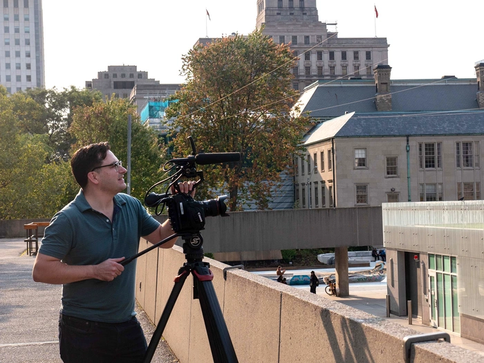 A man in a blue shirt stands on a rooftop and films.