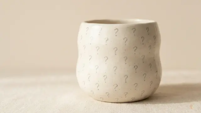 A minimalist ceramic cup with question marks on a neutral linen background, highlighting a Paired app review, daily couples questions, and relationship connection games.