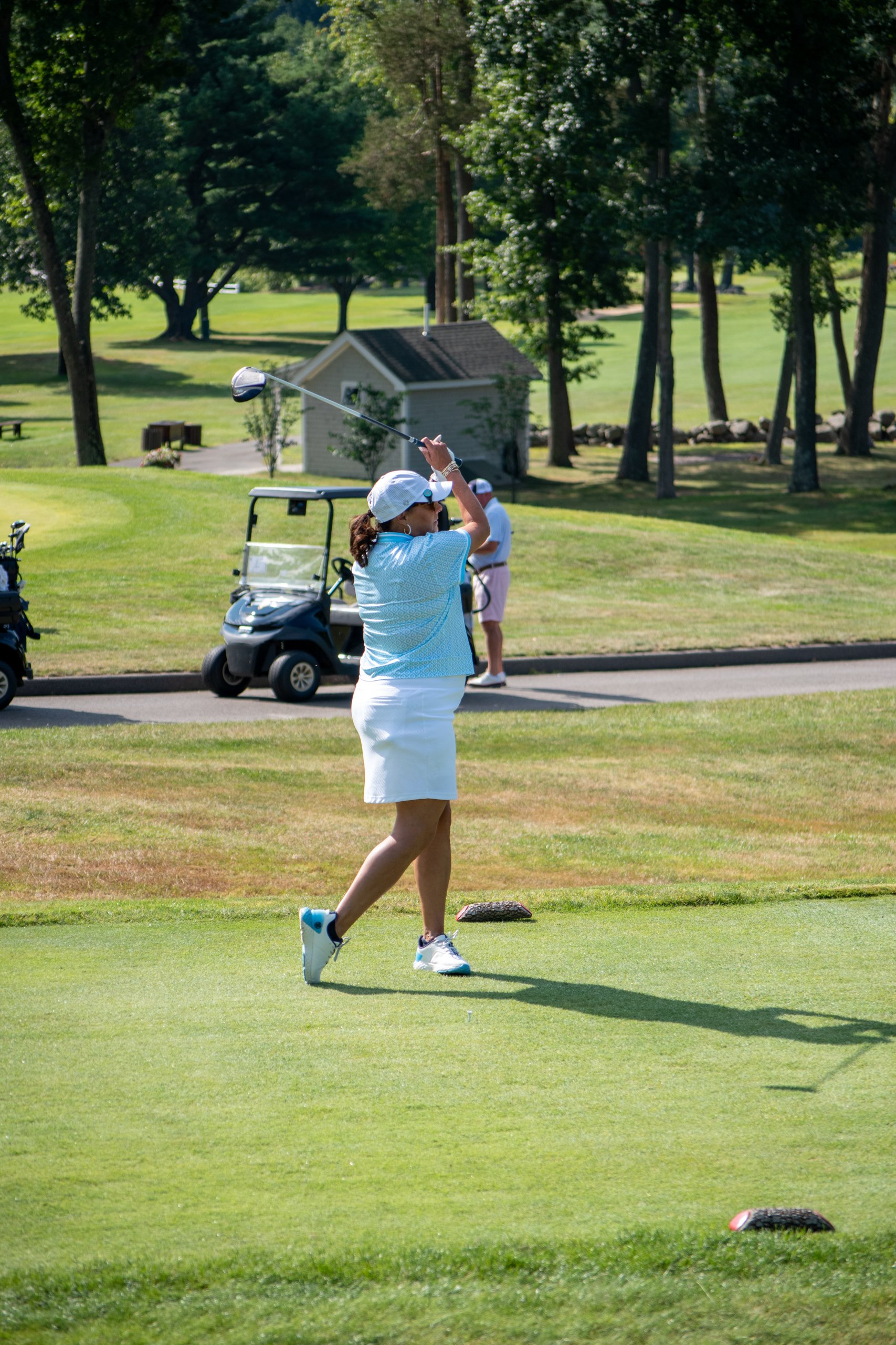 Woman finishing her tee-shot follow-through with the driver over her shoulder, golf cart and course beyond.