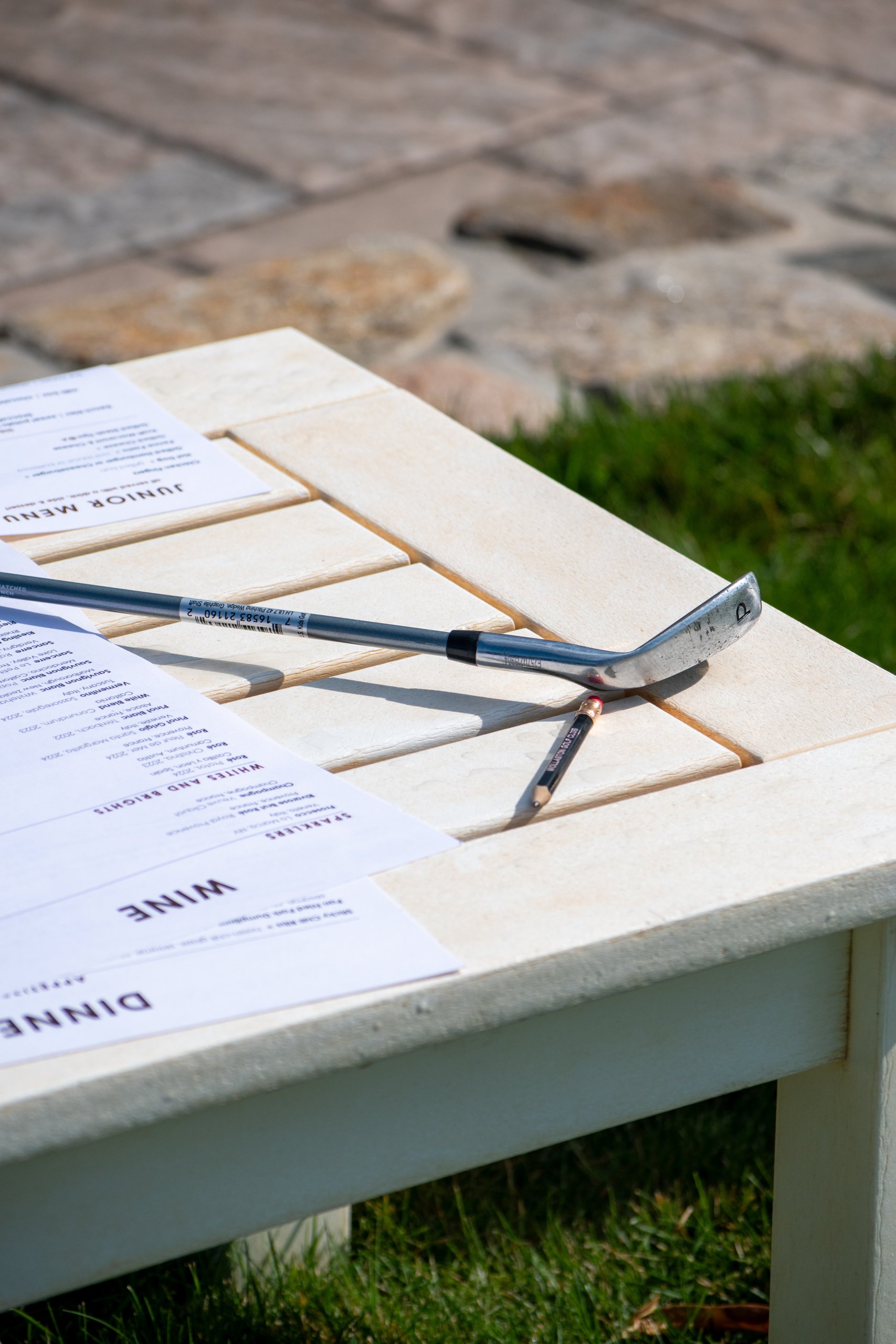 Close-up of a golf wedge and a Williams Golf Club pencil resting on a white table over the dinner, wine and junior menus.
