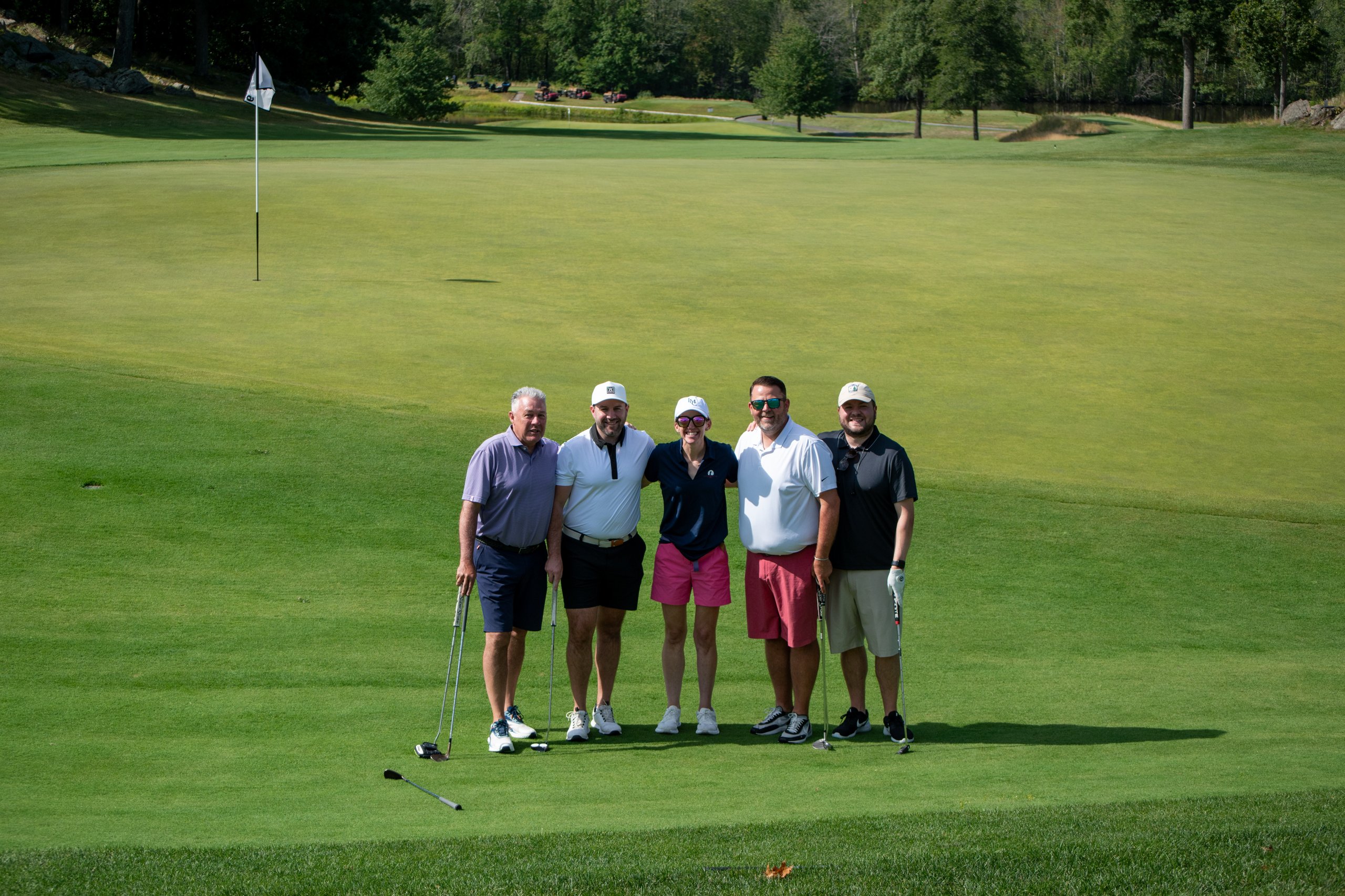 Group of five golfers posing on the green with their putters, the flag to the left and the fairway stretching behind.