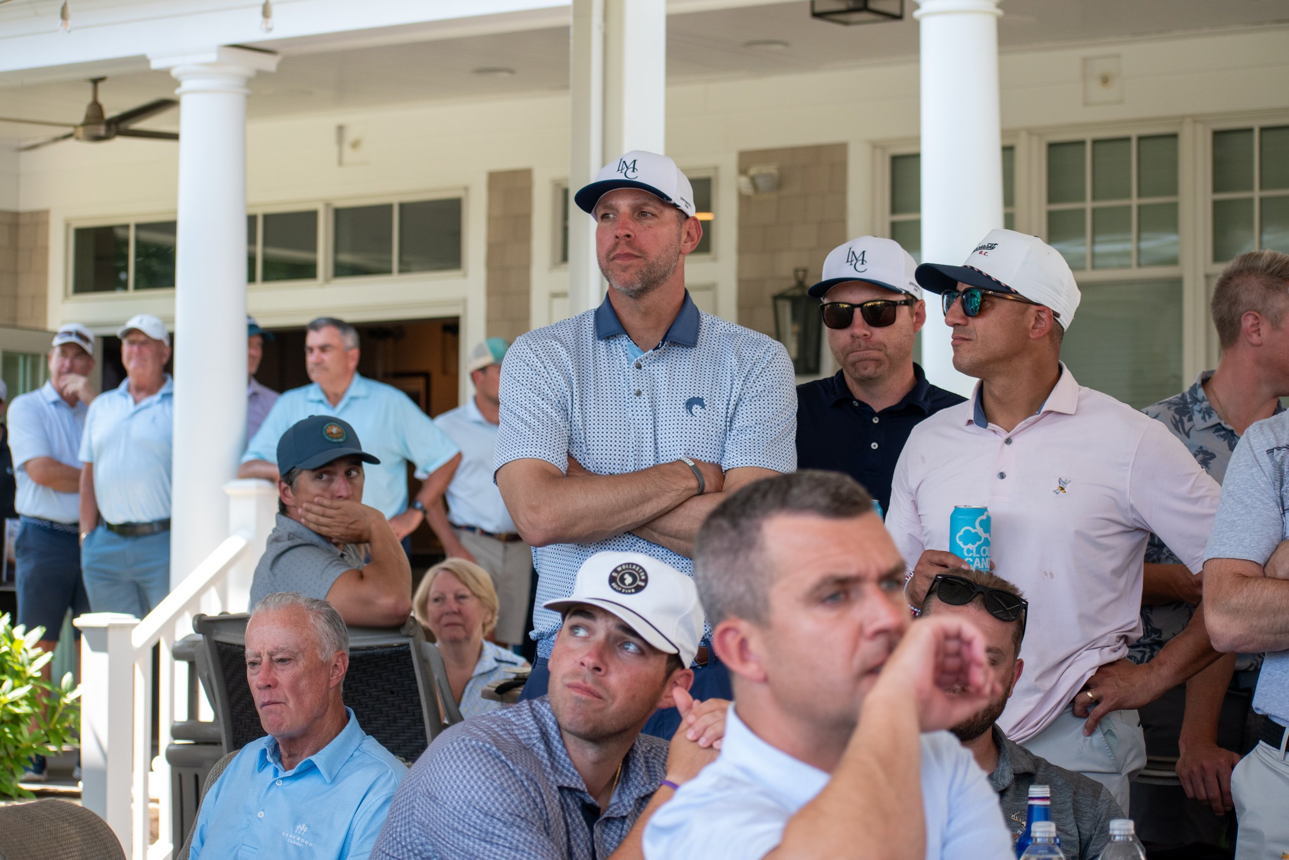 Crowd of golfers and guests gathered on the clubhouse porch watching the awards, several in LMC caps.