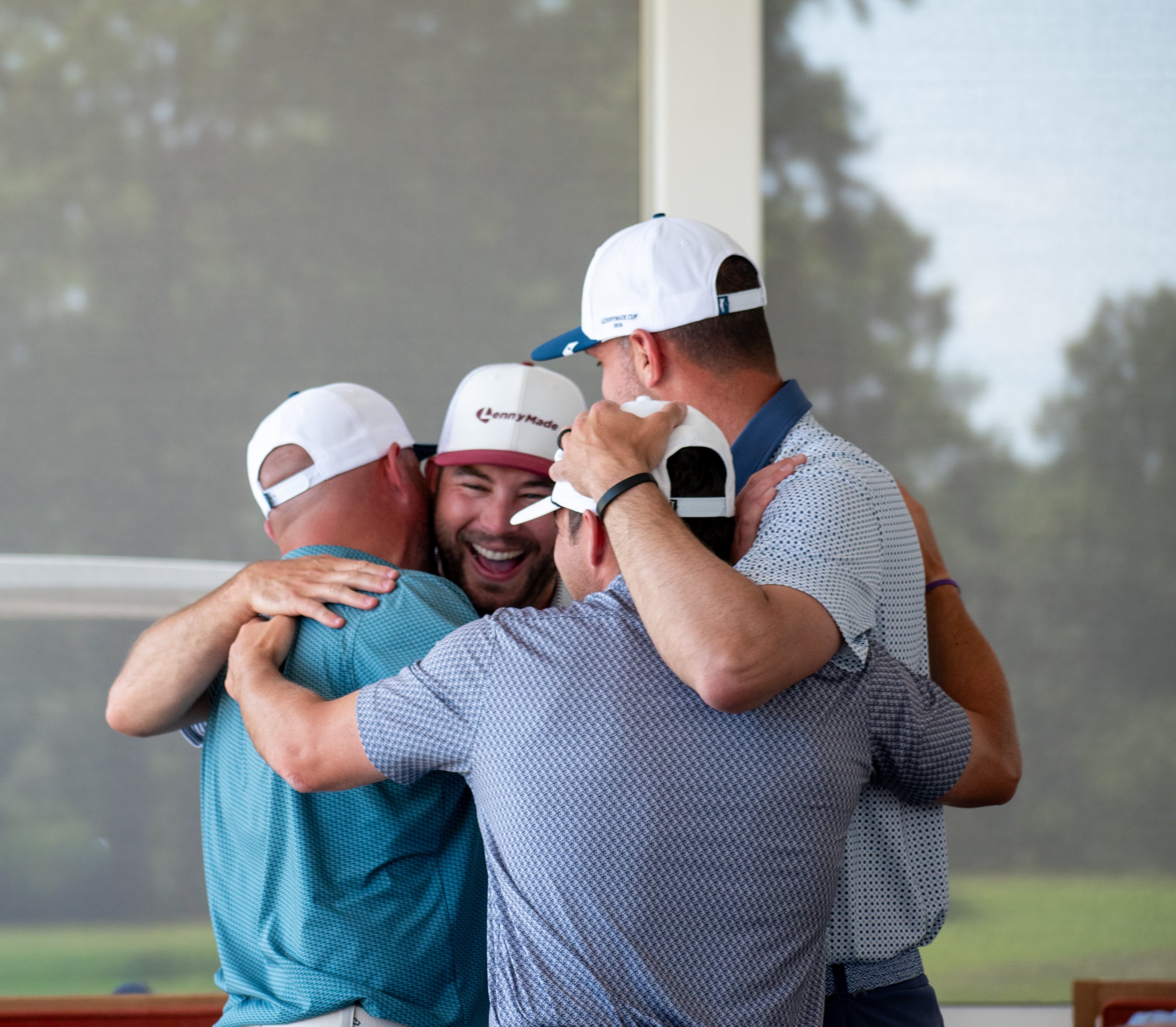 Golfers embracing in a joyful group hug, one grinning in a LennyMade cap, others in LMC hats.