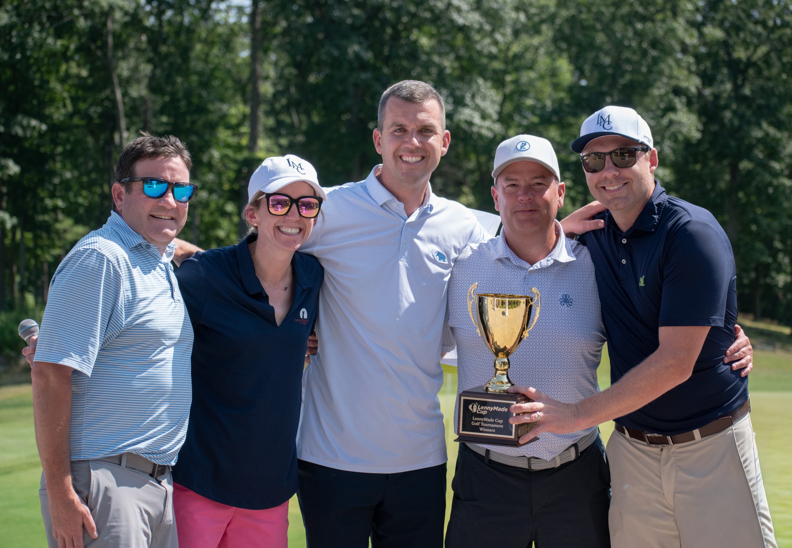 Five winners posing together with the gold LennyMade Cup trophy on the course, smiling for the camera.