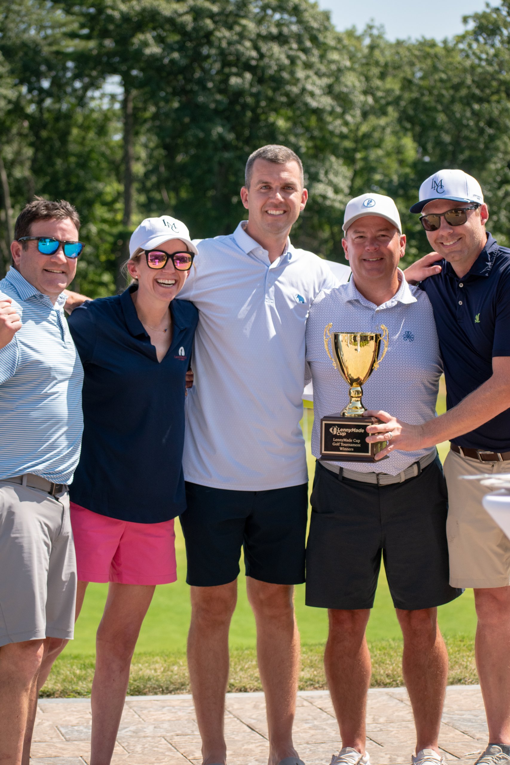 The winning group posing with the LennyMade Cup golf tournament trophy, arms around each other.