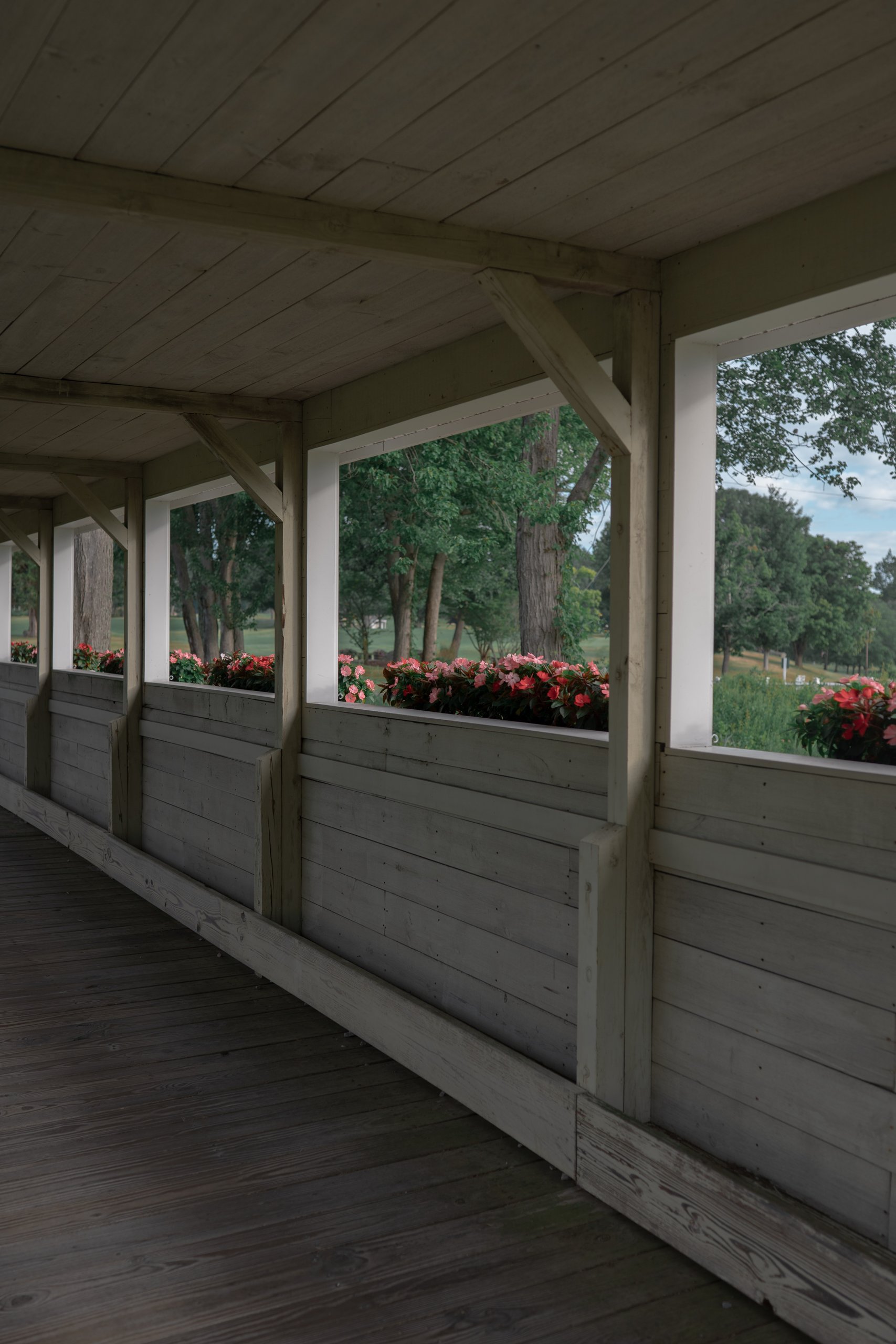 Interior of the covered walkway with open windows and flower boxes of pink and red impatiens overlooking the course.