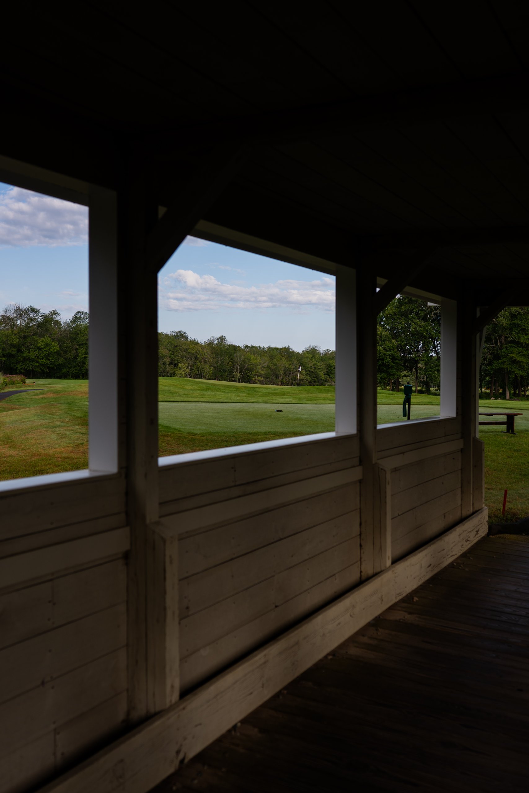 View from inside the covered porch through its windows to a green and flag on the course.