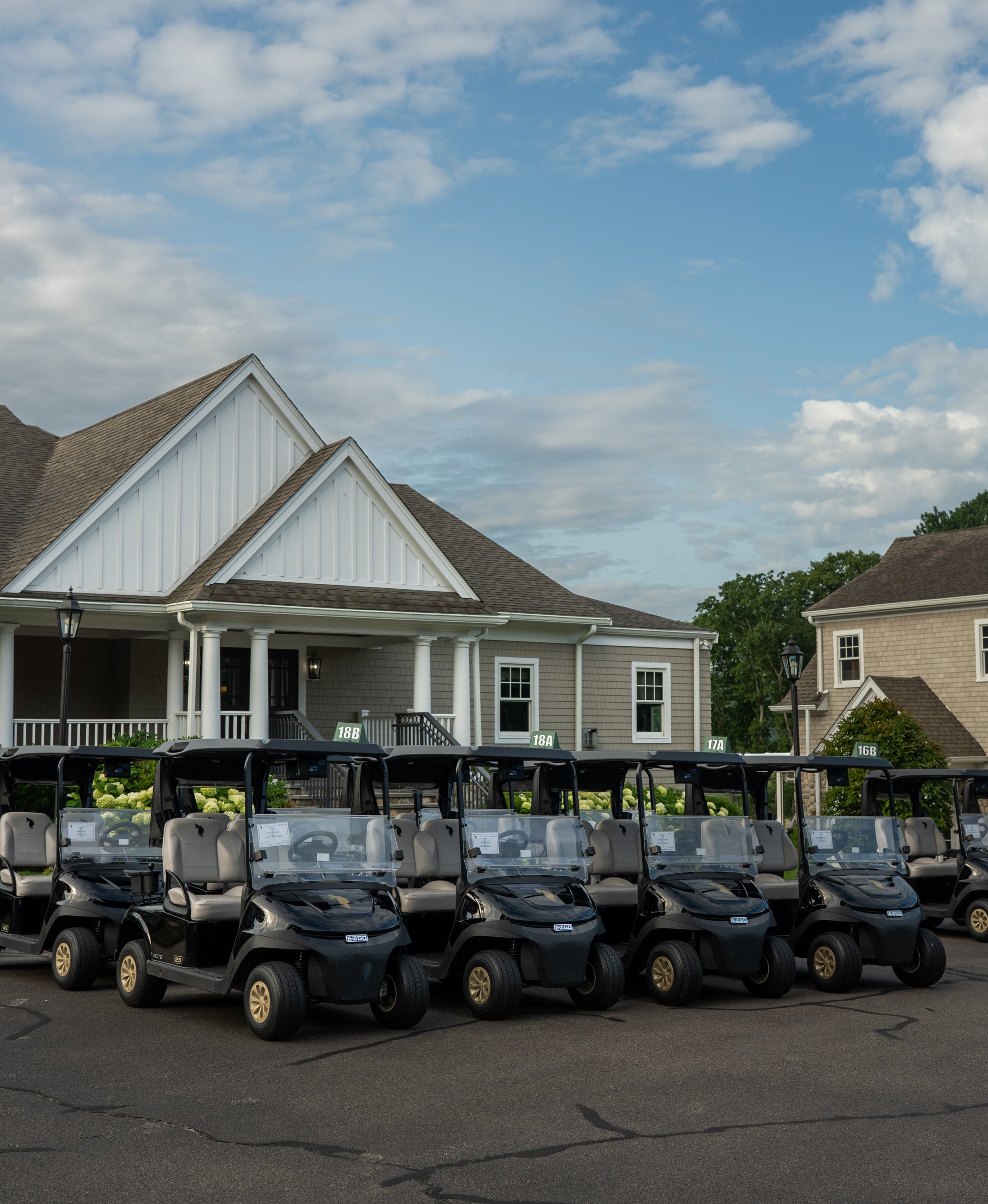 Rows of black EZGO golf carts with numbered hole signs lined up in front of the clubhouse before the shotgun start.