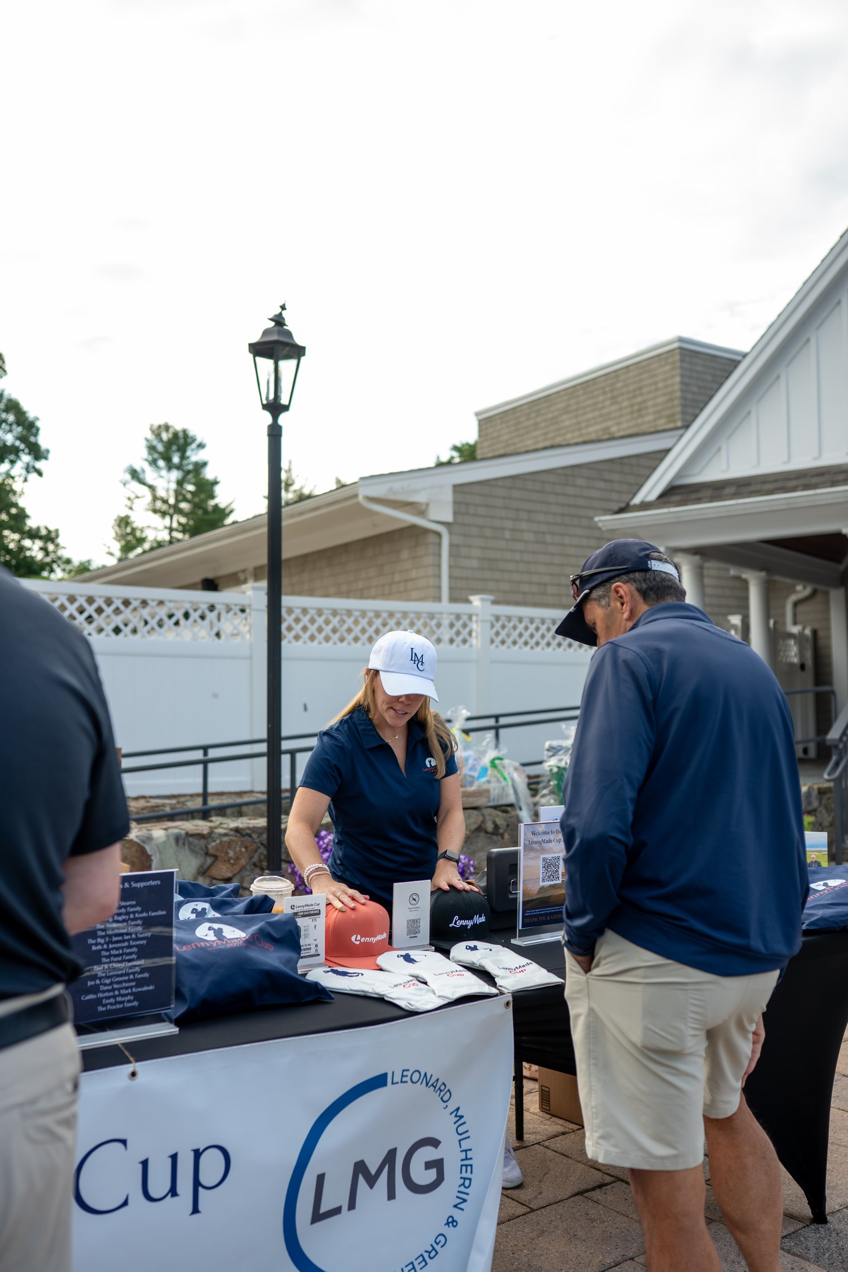 LennyMade Cup merchandise and raffle table staffed by a woman in an LMC cap, with a guest browsing hats.